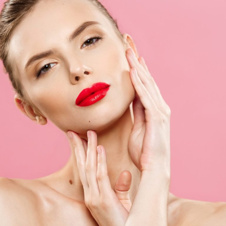 Beauty concept - Gorgeous Young Brunette Woman face portrait. Beauty Model Girl with bright eyebrows, perfect make-up, red lips, touching her face. Isolated on pink background