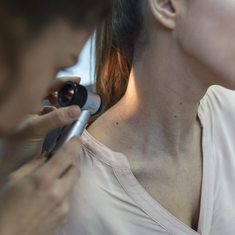 Dermatologist in latex gloves holding dermatoscope while examining attractive patient with skin disease. Female dermatologist examining patient with dermascope, looking for signs of skin cancer.