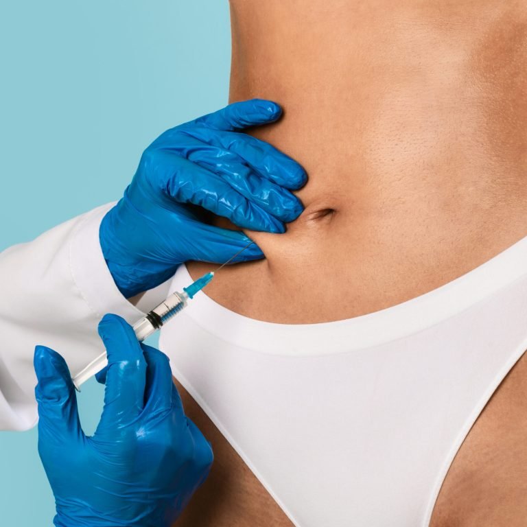 Plastic surgeon in protective gloves making injection at belly area for unrecognizable lady, blue studio background. Slim woman having lipolysis treatment at beauty salon, cropped close up view